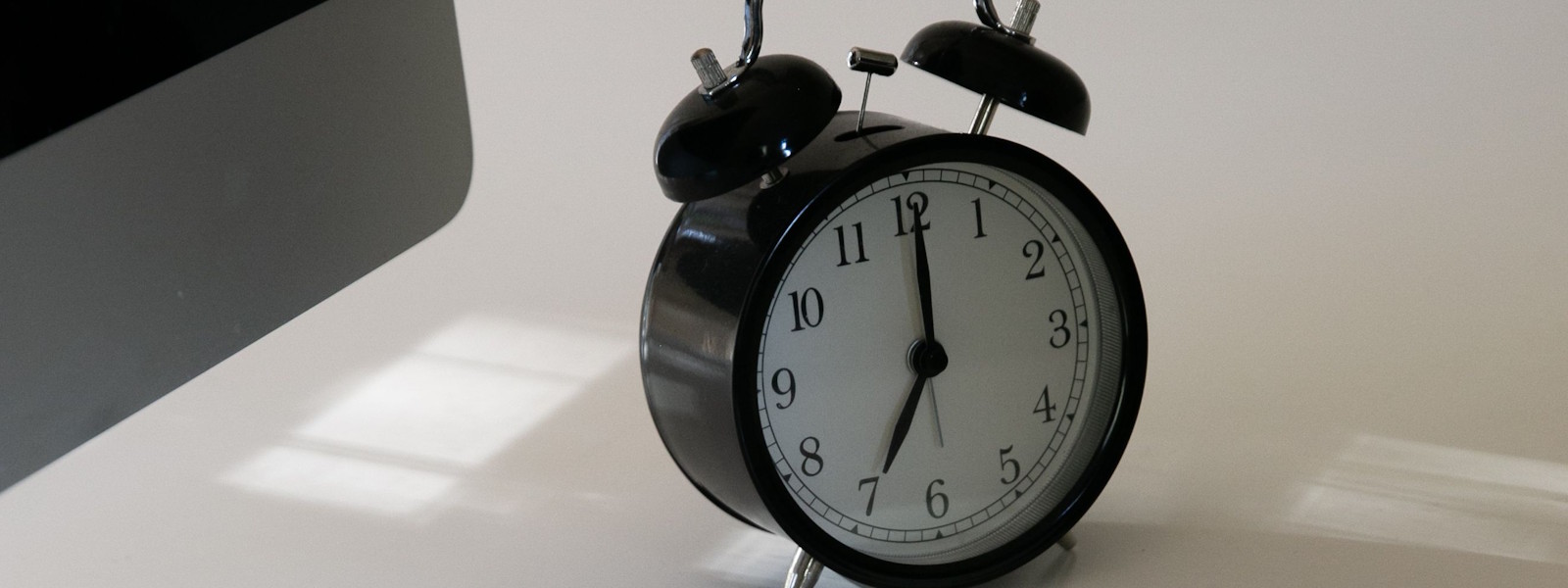 A black alarm clock standing on an office desk beside a computer keyboard