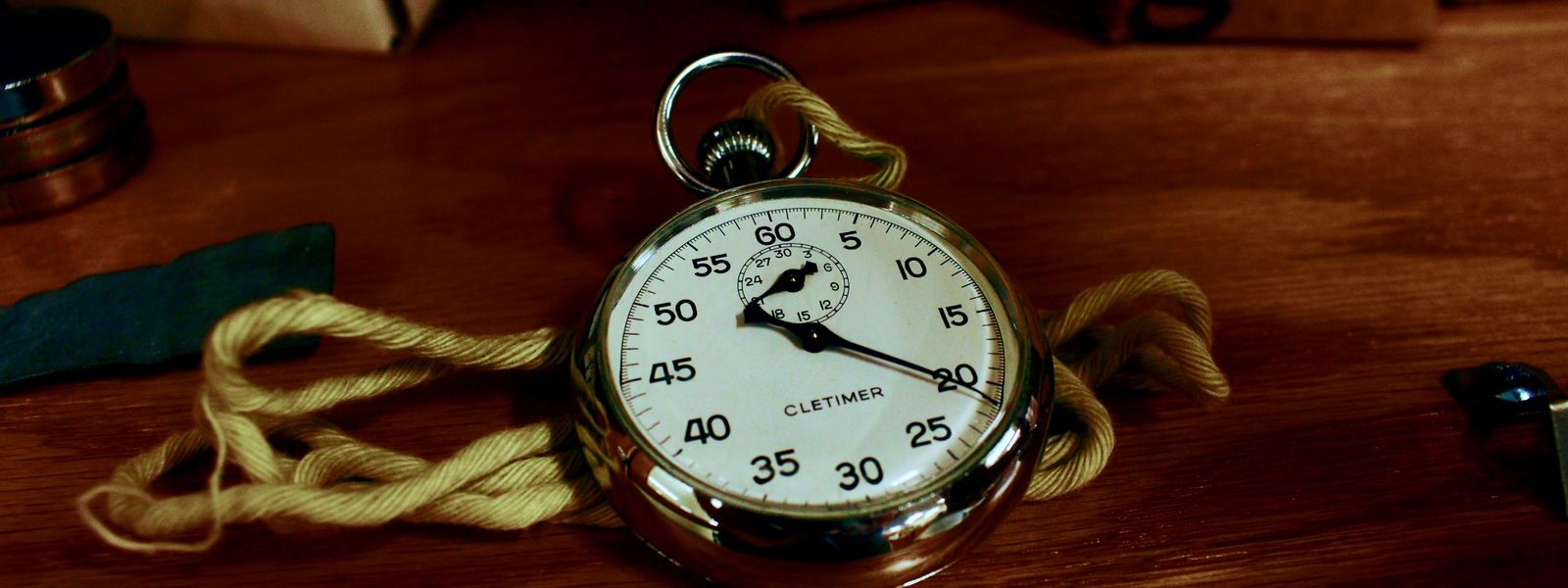 An antique silver analog stopwatch lying on a wooden table beside a coiled rope