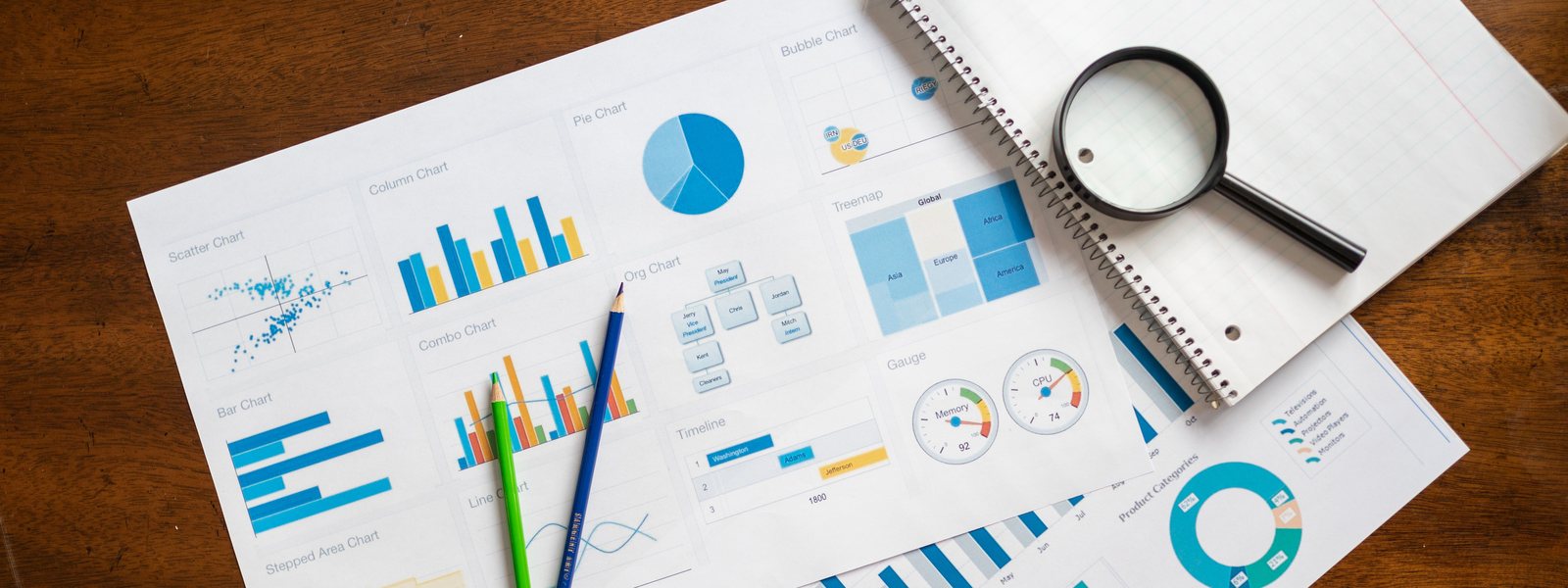 Printed sheets of pie and bar charts spread across a dark wooden table beside two pencils and a magnifying glass resting on a spiral notepad