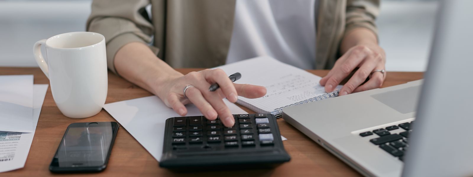 Person using a calculator beside a laptop while working through invoices and paperwork at a desk