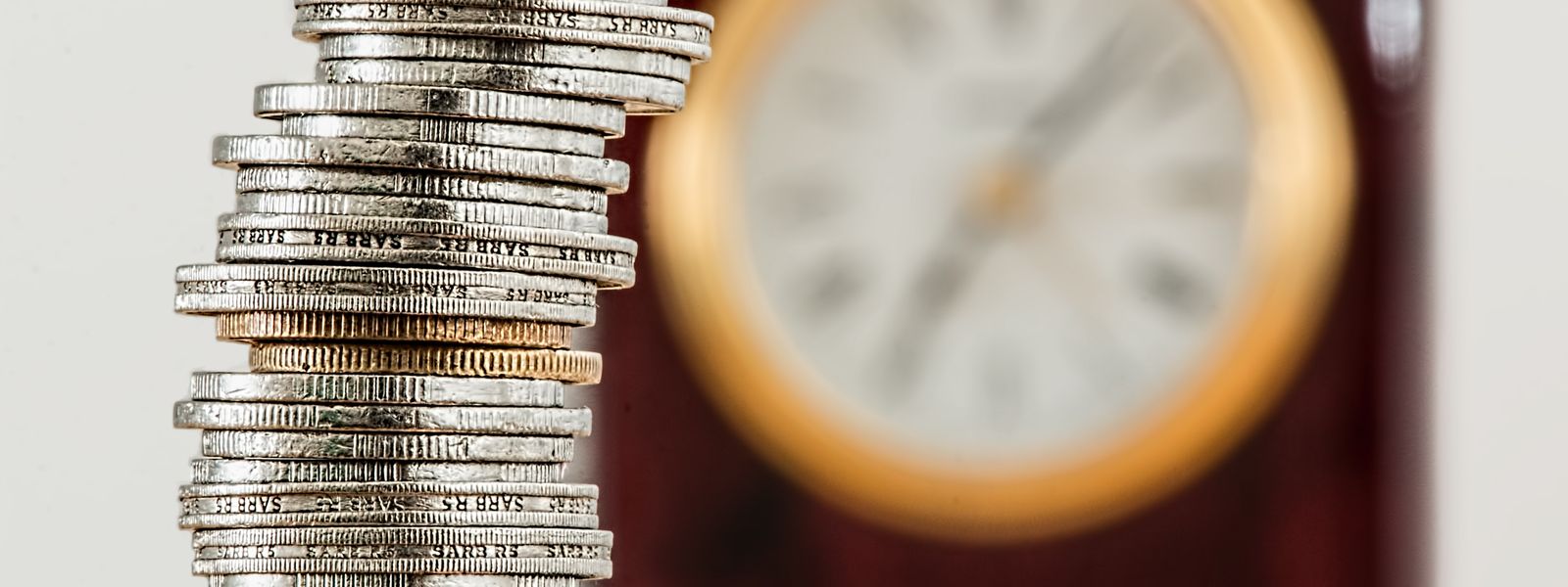Stack of silver and gold coins in front of a blurred clock face
