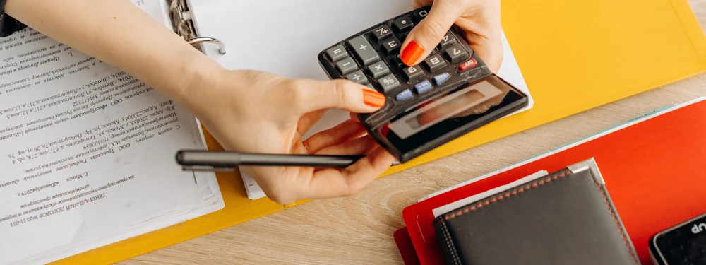 Hands using a calculator beside printed documents on a desk