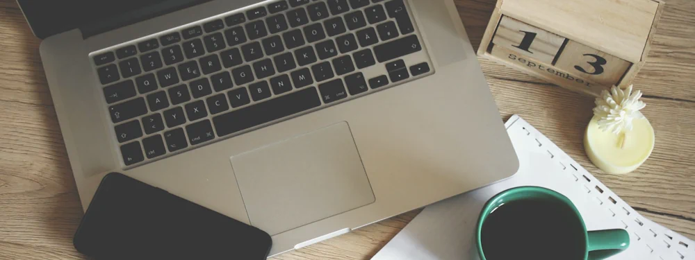 A tidy desk with a laptop, smartphone, coffee and a wall calendar
