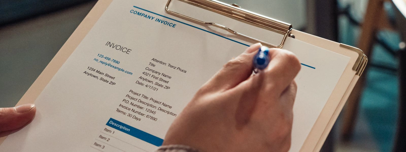 A hand holding a printed invoice on a clipboard with a pen
