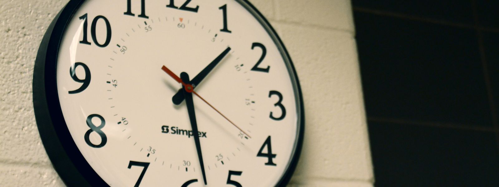 Round black analog wall clock on a white brick wall