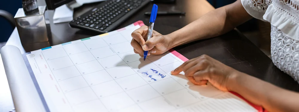 A person marking dates on a wall calendar with a marker pen