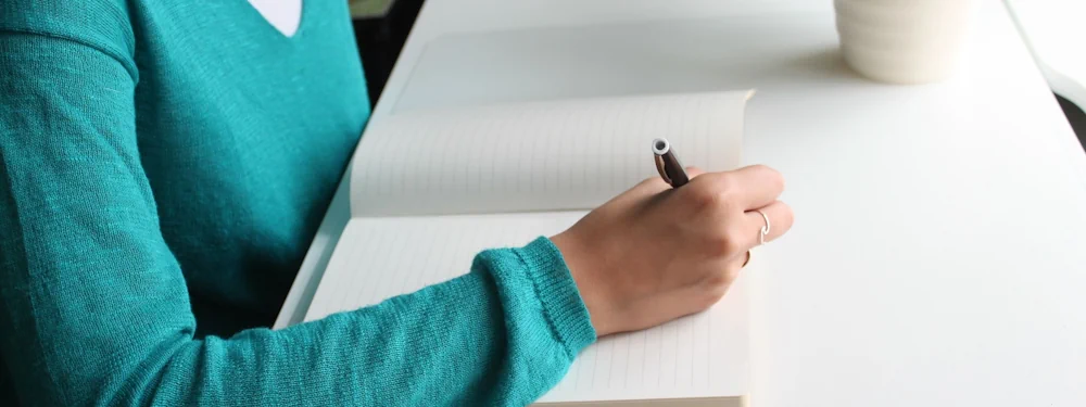A person writing notes by hand in a notebook at a desk
